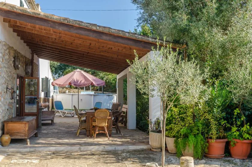 A covered outdoor patio with a dining table, seating, and potted plants.
