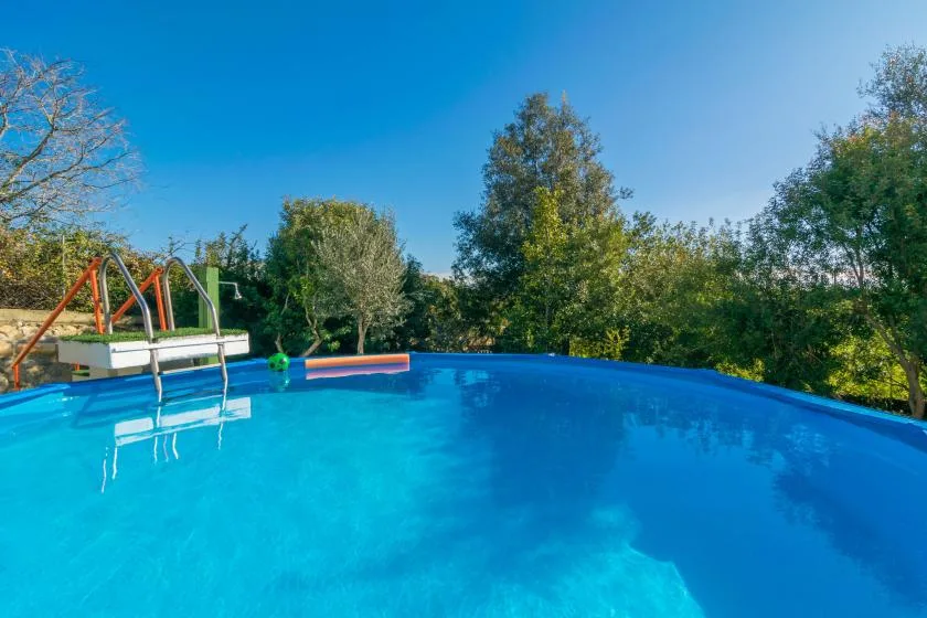 An outdoor swimming pool with a small slide and trees beyond.