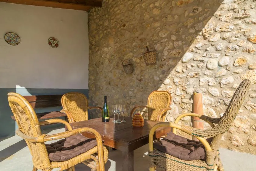 A stone-walled patio with wicker seating around a wooden table.