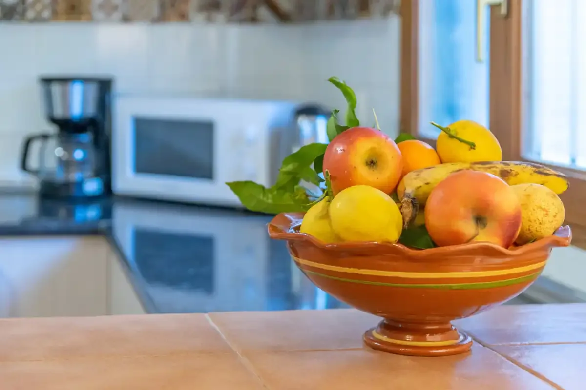 Kitchen counter with a bowl of assorted fruit in front of small appliances.