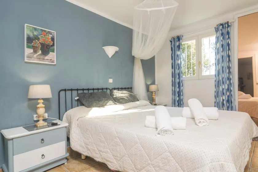 A bedroom with a large bed, blue walls, and patterned curtains beside the window.