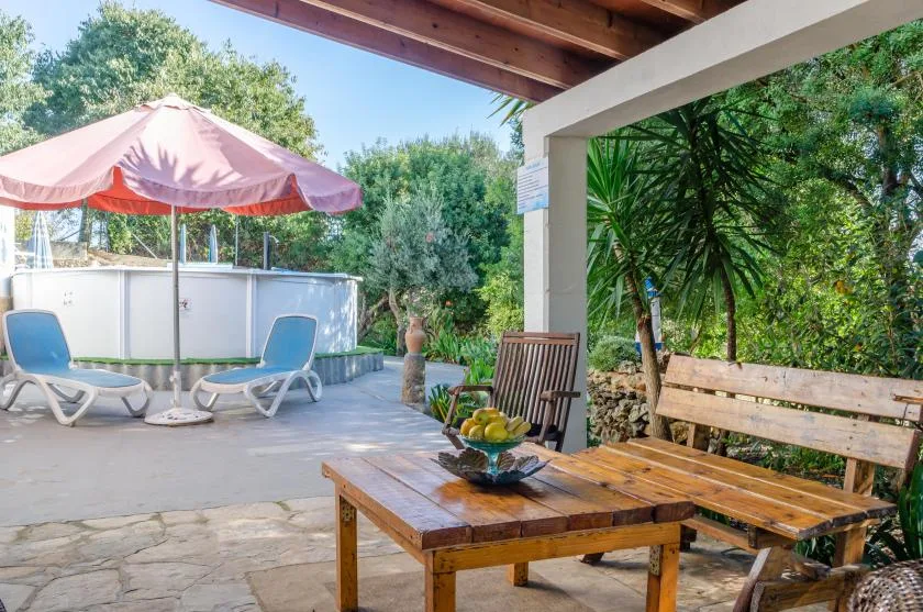 A covered outdoor patio with a wooden table and seating beside a garden.