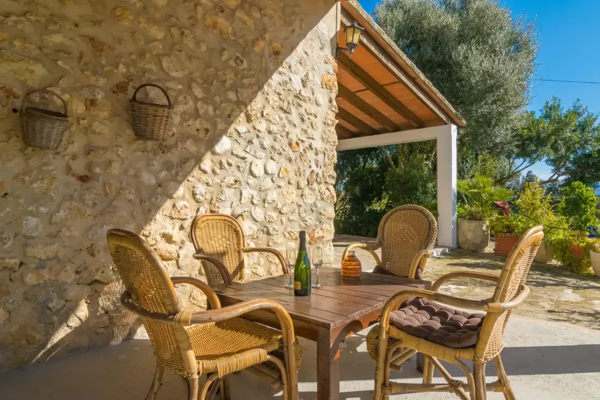 A stone patio with wicker seating and a wooden table beneath a covered terrace.