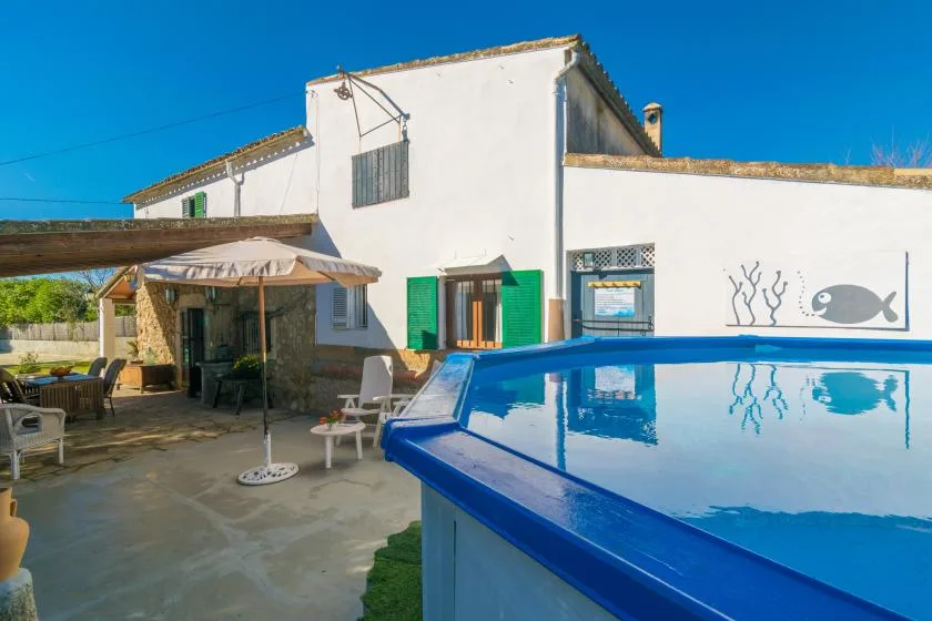 A white house beside a blue swimming pool, with shaded outdoor seating.