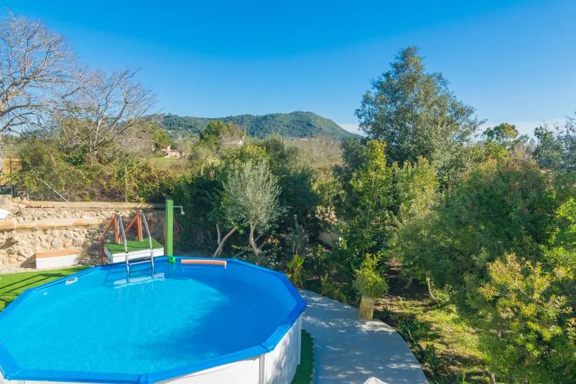An outdoor swimming pool sits beside a paved path, with trees and hills beyond.