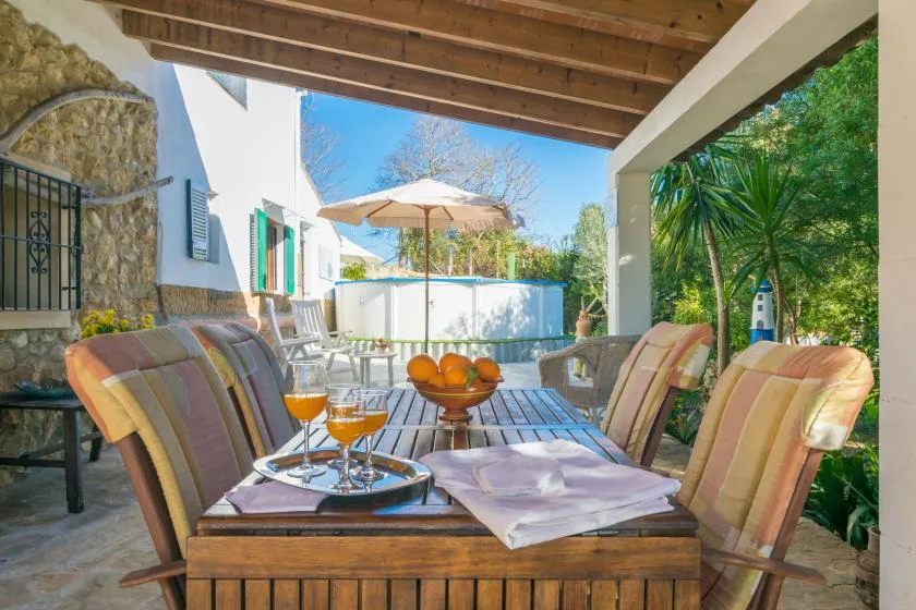 A covered patio with cushioned seating and a table set with drinks and fruit.