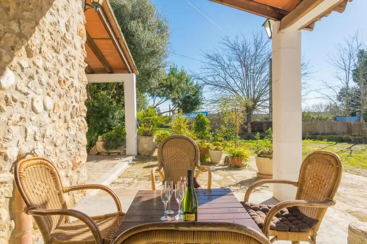 A covered outdoor dining area with wicker seating overlooks a garden.