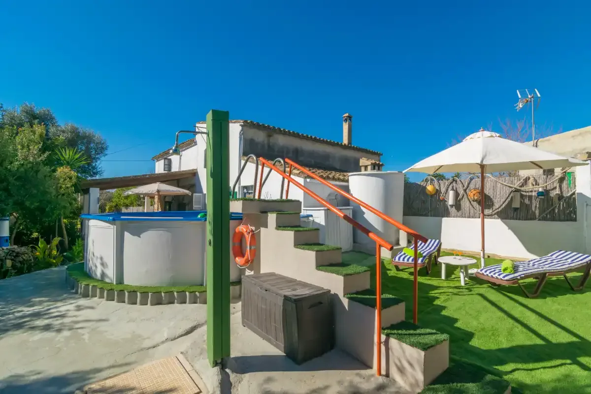 An outdoor pool area with steps and sun loungers on the grass.