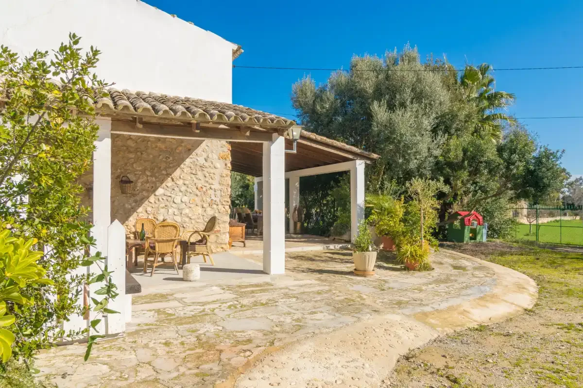 A stone patio beside a house is shaded by a covered seating area.