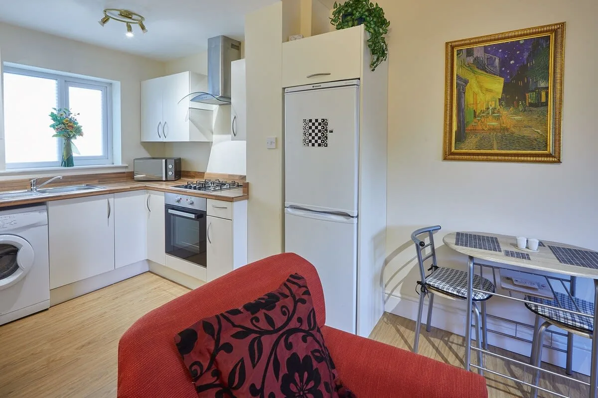 Una cocina compacta con comedor, armarios blancos y una mesa junto a la ventana.