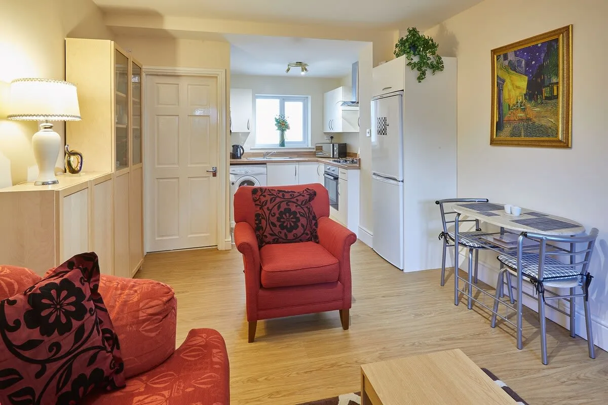 Una sala de estar con asientos rojos junto a una mesa de comedor y una cocina compacta.