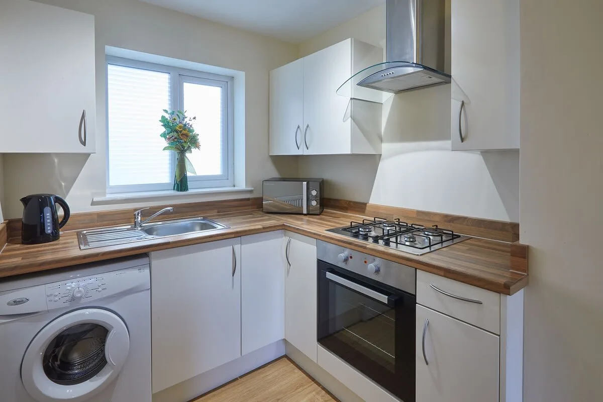 Una cocina compacta con armarios blancos, encimeras de madera y una ventana.
