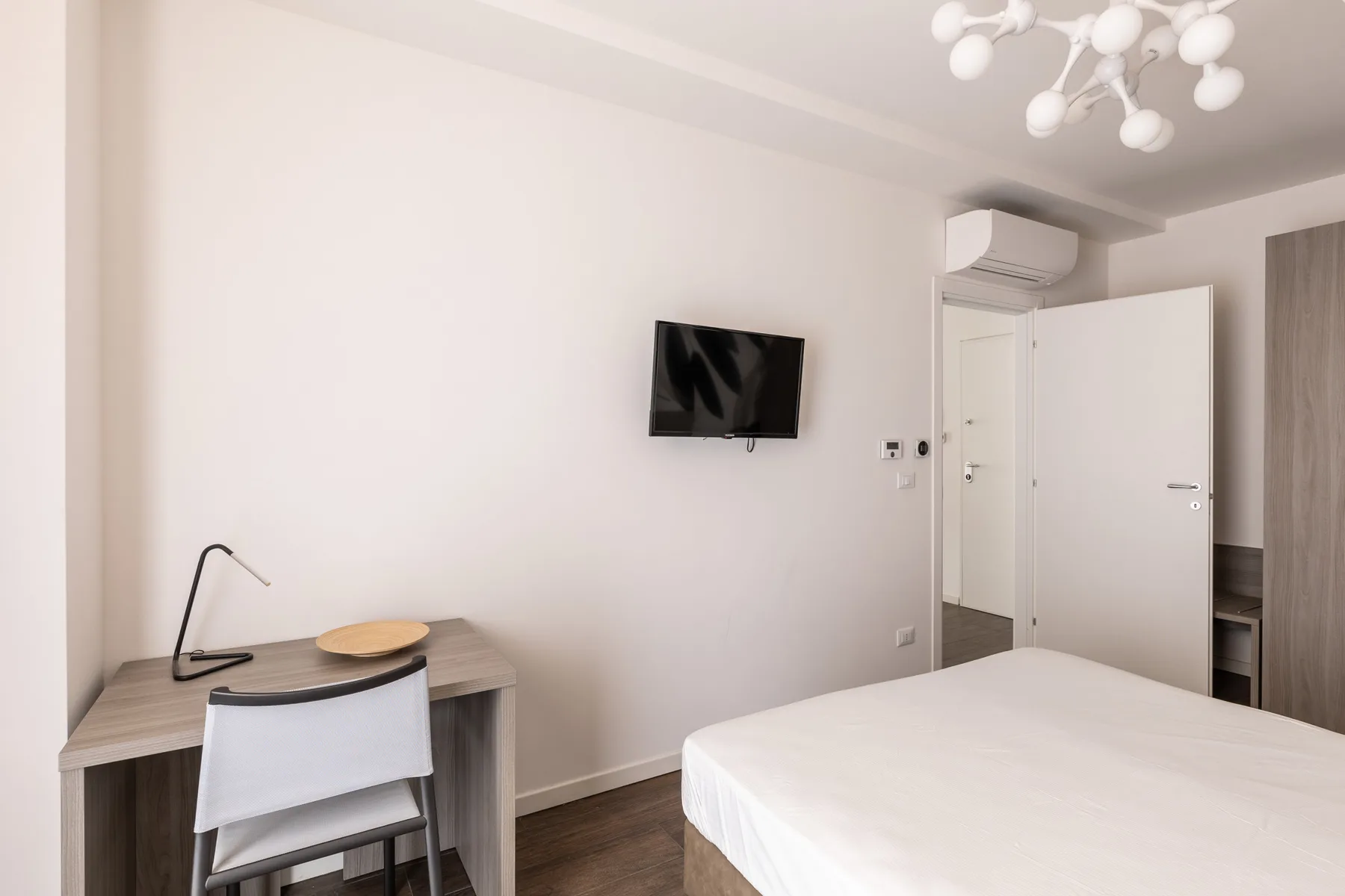 Un dormitorio con cama, escritorio y televisor en la pared.