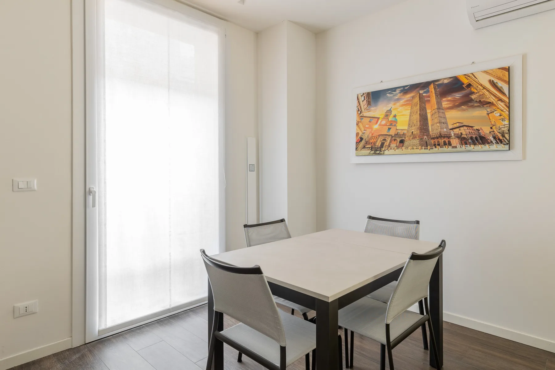 Un comedor luminoso con una mesa, sillas y una obra enmarcada en la pared.