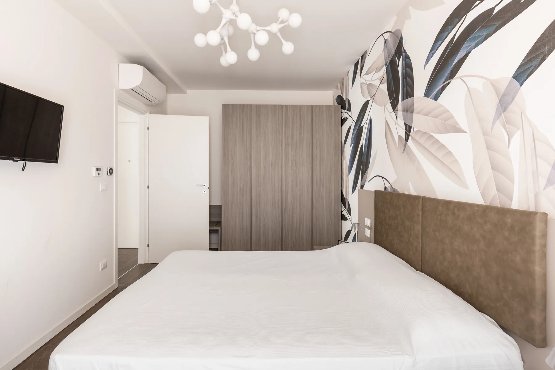 Un dormitorio con una cama grande, un televisor de pared y arte botánico.