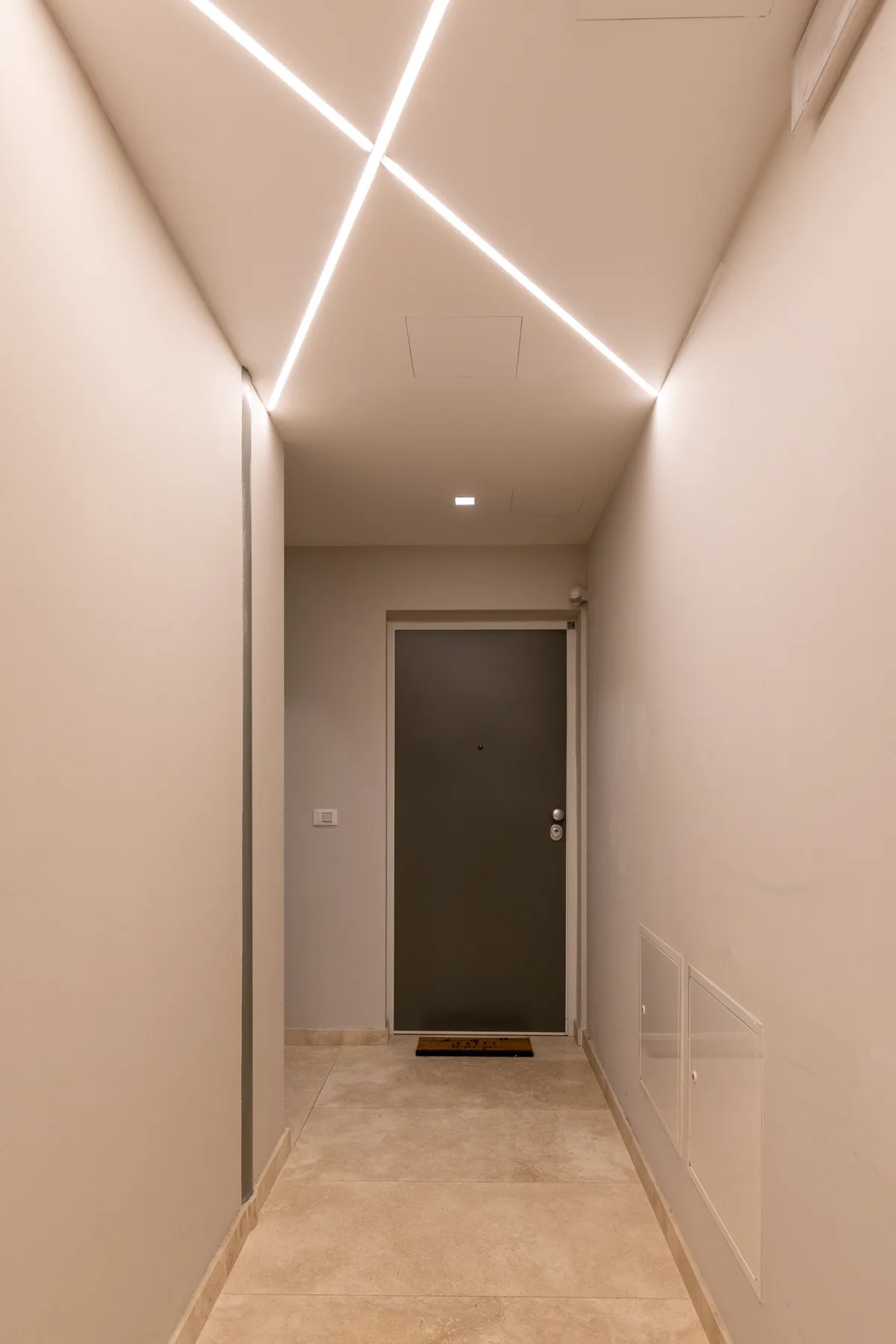 Un pasillo interior estrecho conduce a una puerta oscura bajo luces brillantes en el techo.