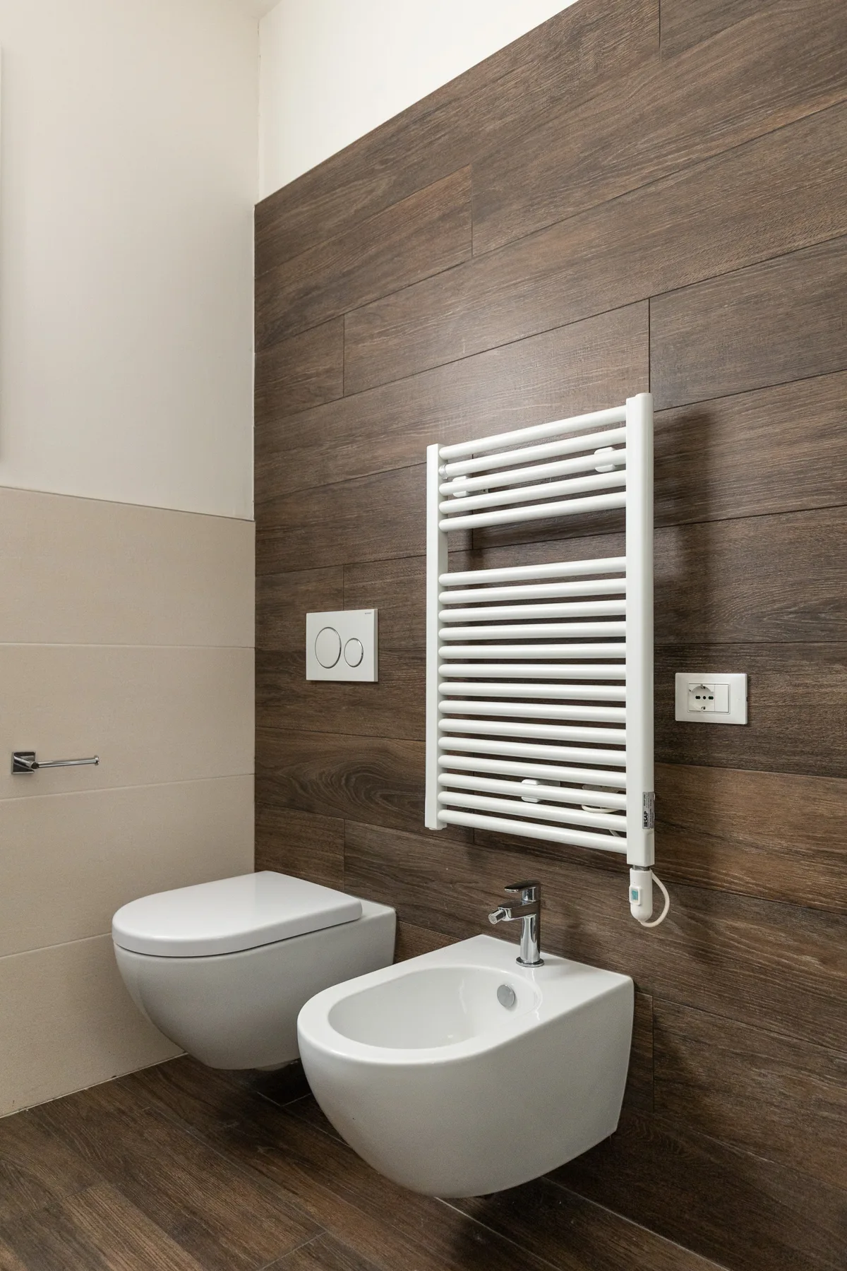 Un baño con inodoro y bidé suspendidos frente a una pared revestida de madera.