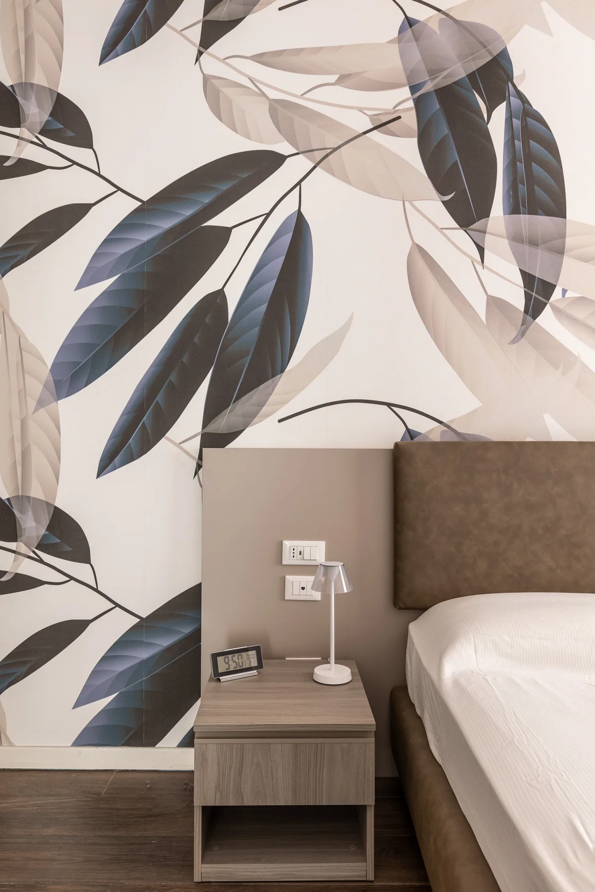 Un dormitorio con una cama junto a una mesita de noche y papel tapiz de hojas llamativas.