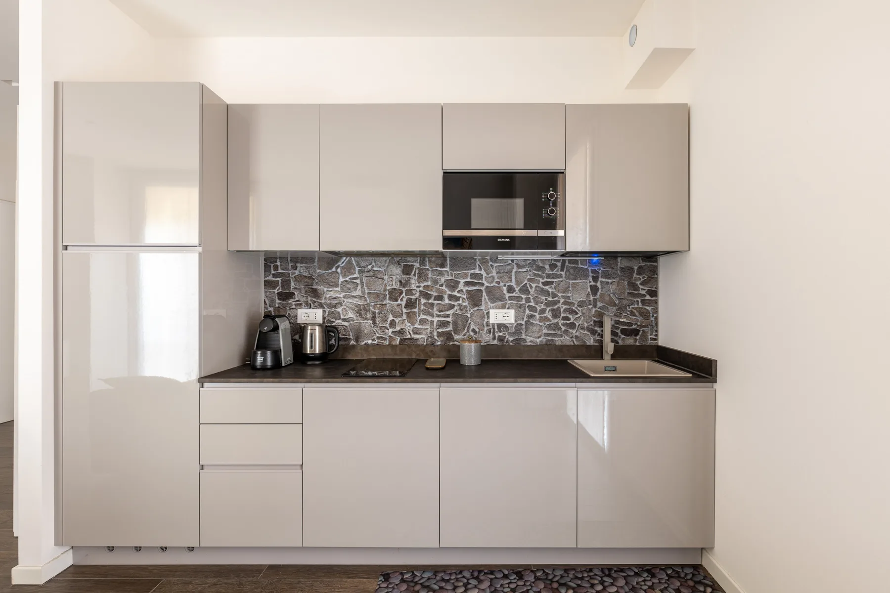 Una cocina moderna con gabinetes claros y un salpicadero oscuro de piedra.