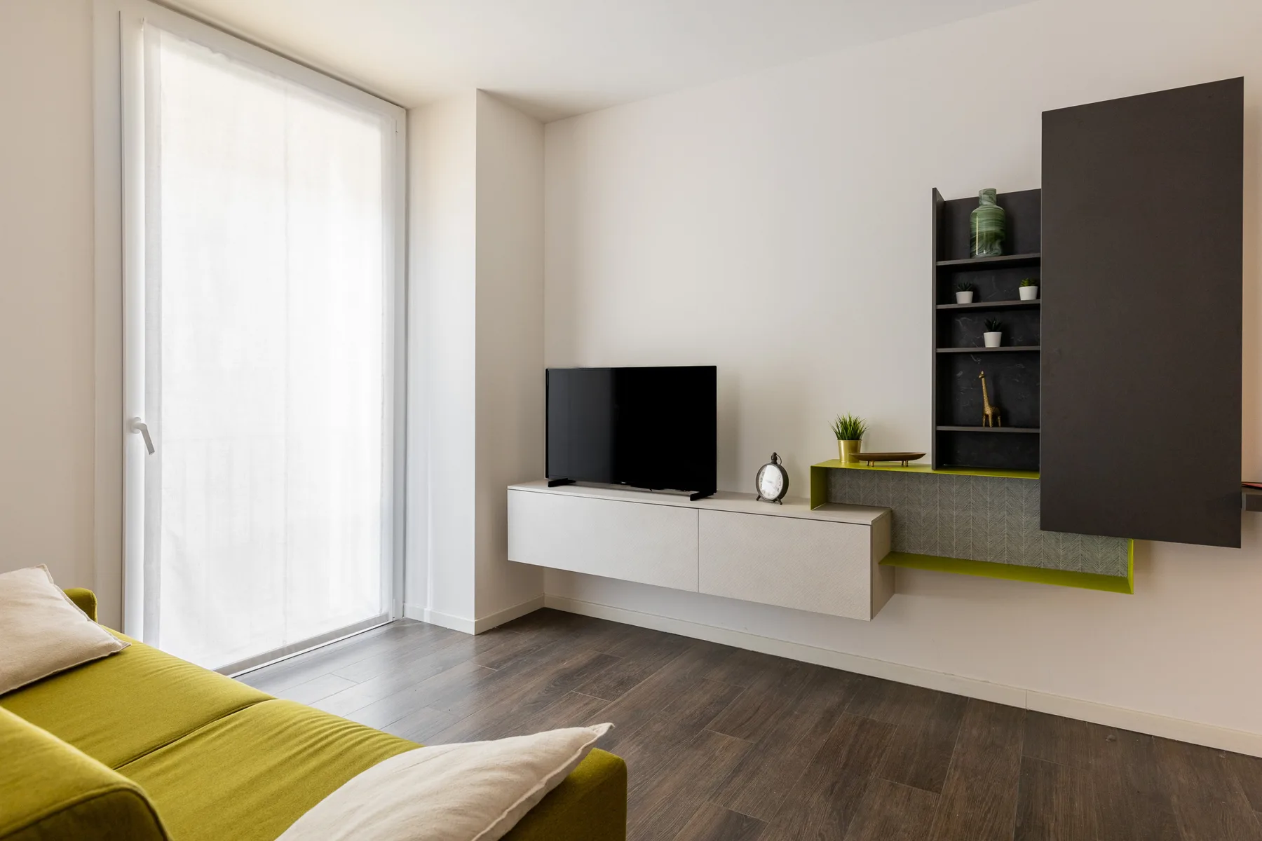Una sala de estar moderna con televisor, mueble flotante y asientos verdes.
