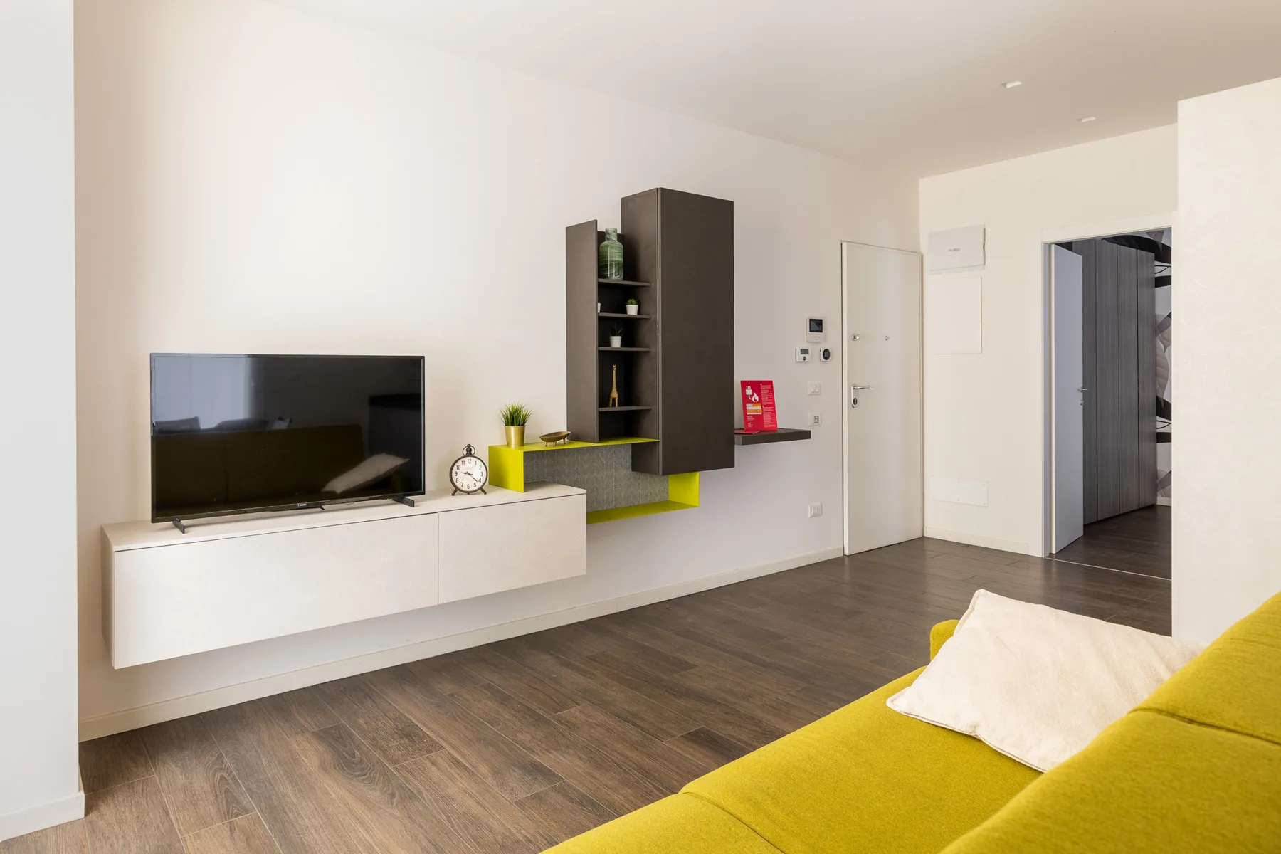 A living room with a television mounted above a floating cabinet and yellow seating.