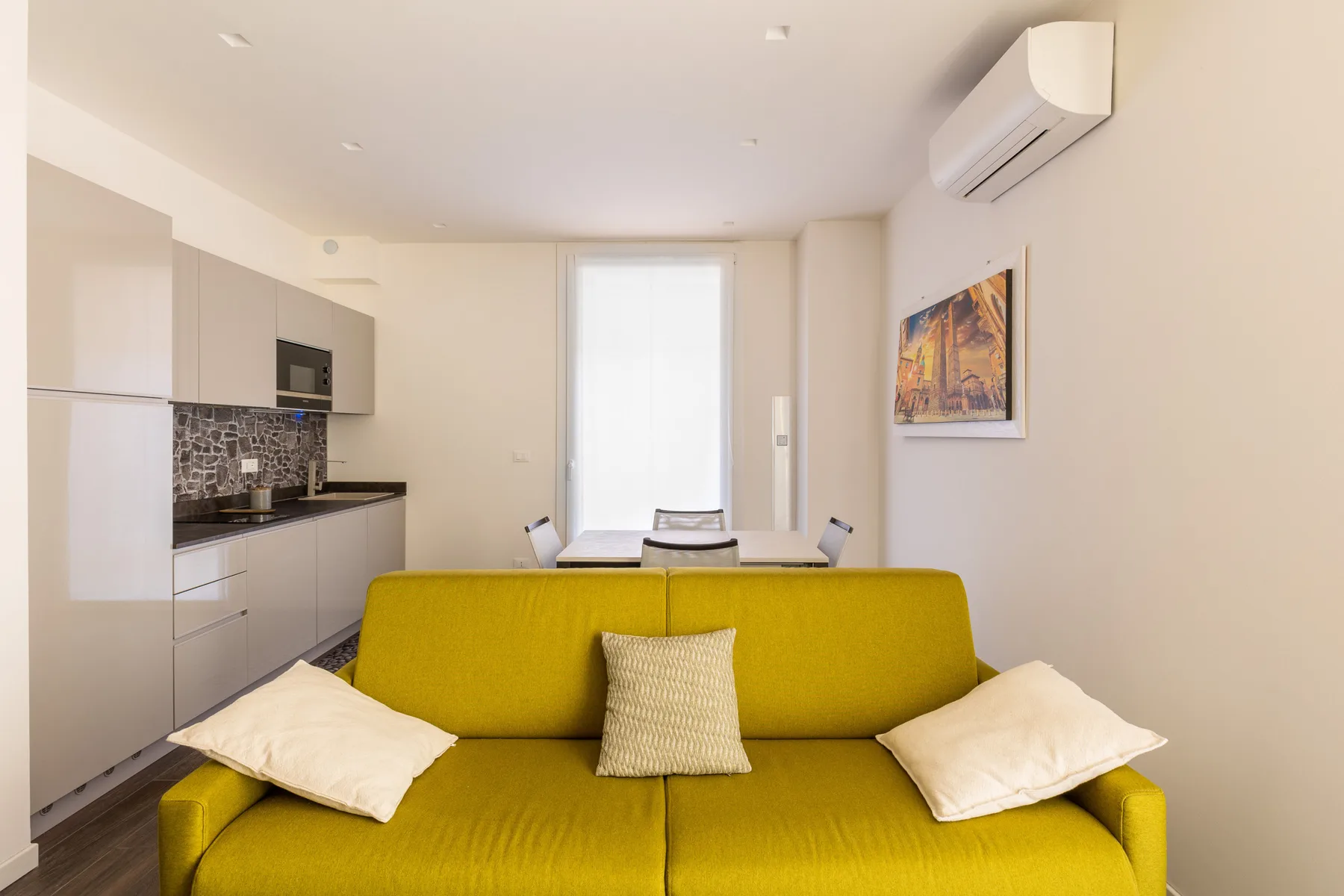 A bright living area with a yellow sofa, dining table, and compact kitchen.