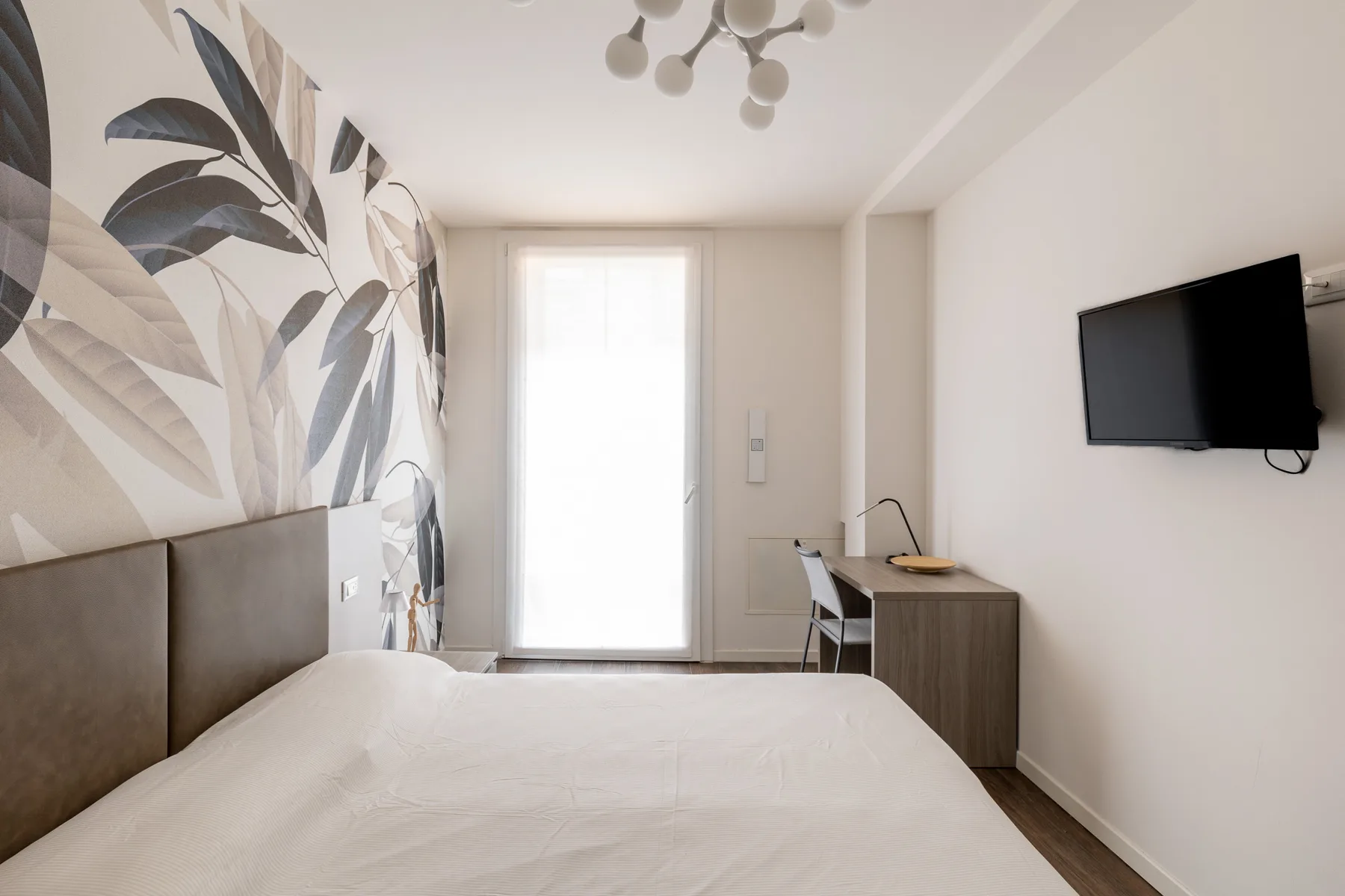 Un dormitorio con una cama, un televisor en la pared y un gran mural botánico.