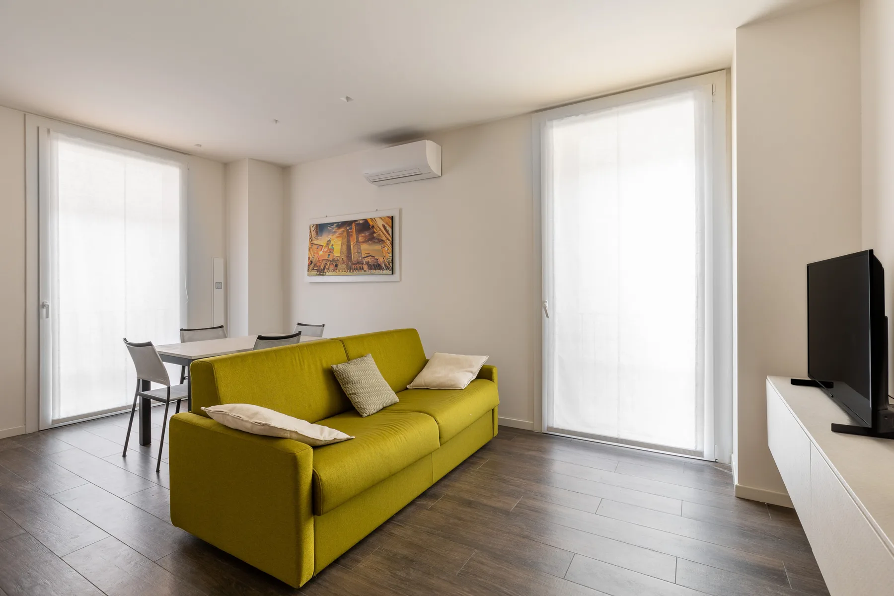 A bright living room with a green sofa, dining table, and large windows.