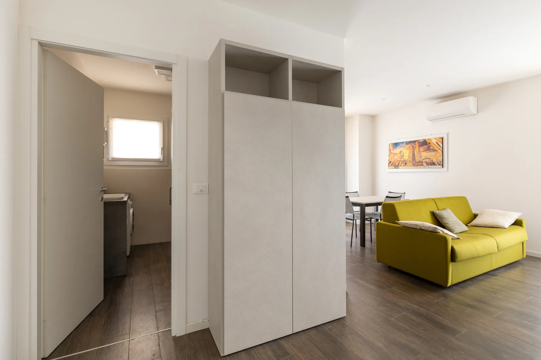 Una sala luminosa con un sofá verde junto a una cocina abierta.