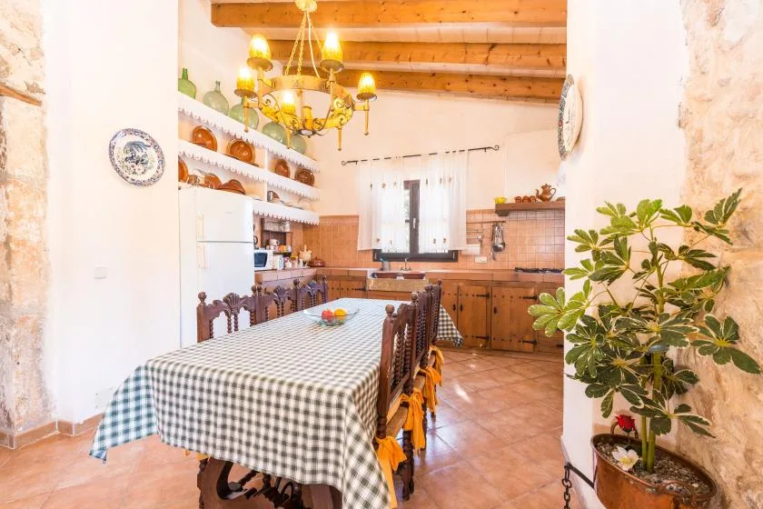 Una mesa de comedor ocupa el primer plano de una cocina rústica con gabinetes de madera.