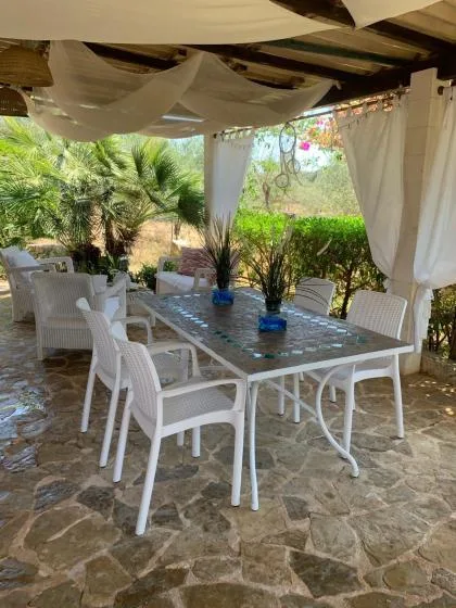 Una zona de comedor exterior a la sombra tiene una mesa y asientos blancos bajo telas drapeadas.