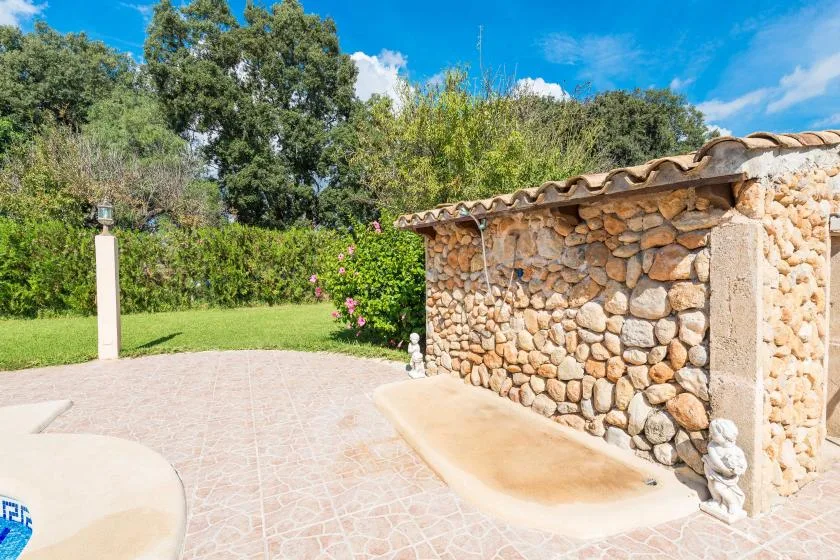 Un patio soleado al aire libre con un muro de piedra curvo y suelo pavimentado.