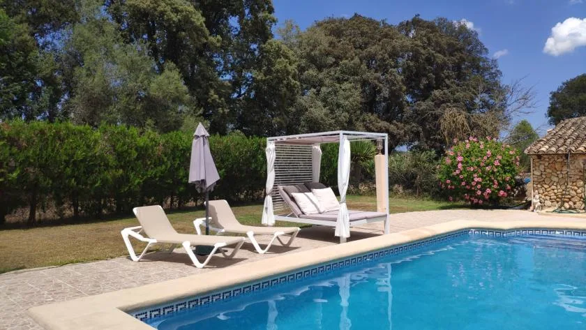 Una piscina al aire libre con asientos reclinables y una cama de día a la sombra.