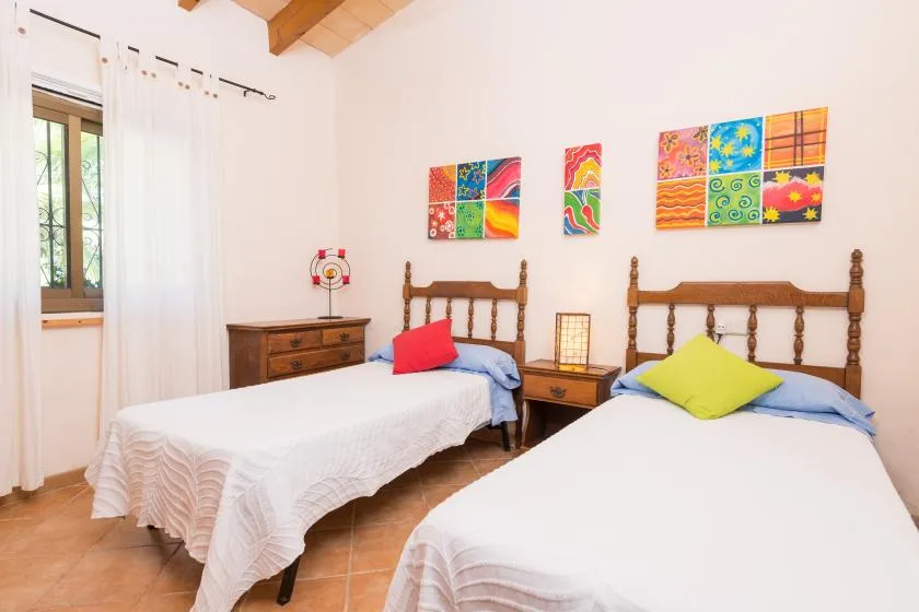 Un dormitorio con dos camas, cuadros coloridos y una ventana.