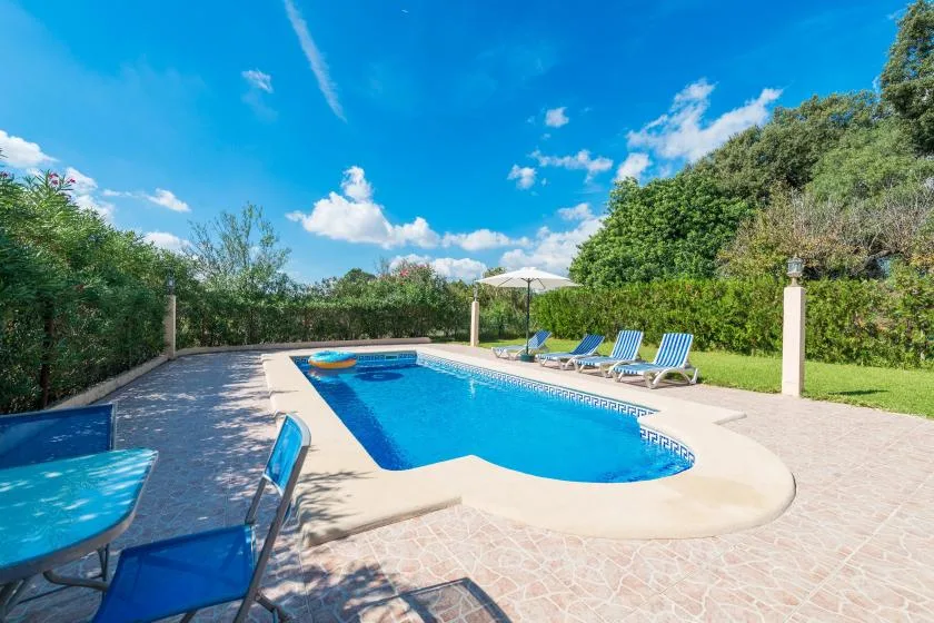 Una piscina al aire libre rodeada de asientos en el patio y vegetación.