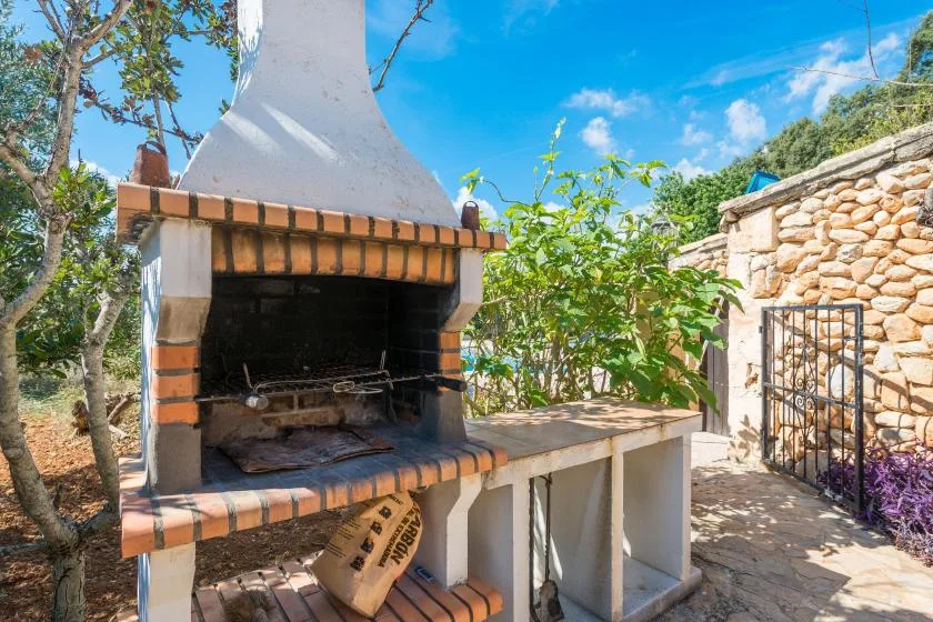 Una barbacoa exterior de ladrillo junto a un muro de piedra y un jardín frondoso.