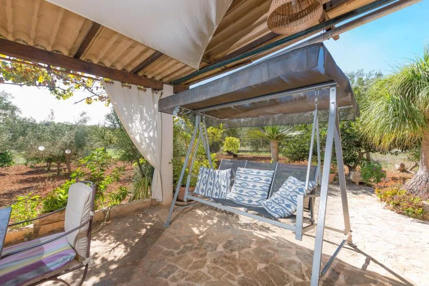 Un patio exterior sombreado cuenta con un columpio acolchado y vistas al jardín.