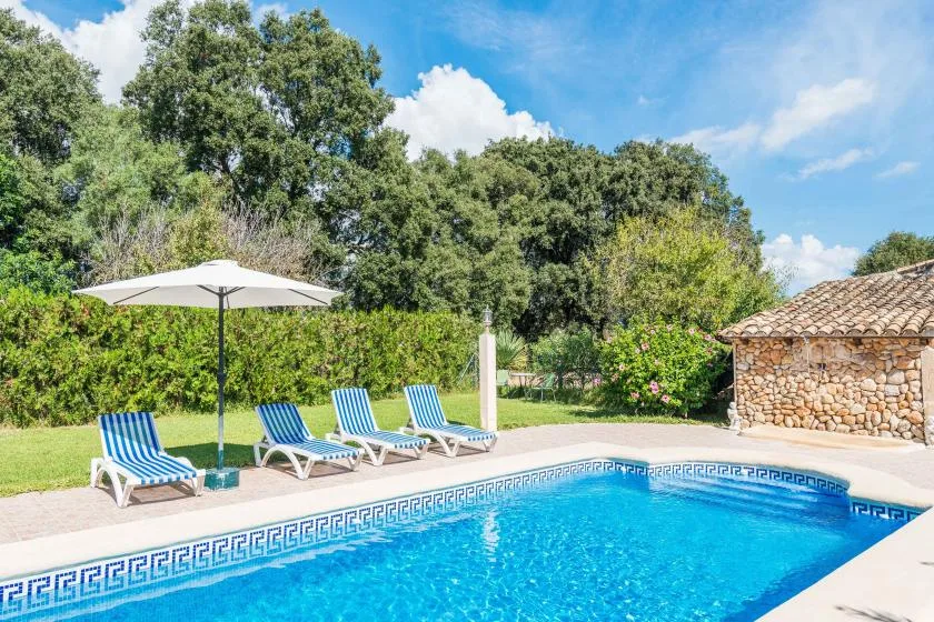 Una piscina al aire libre junto a asientos reclinables y un muro de piedra.