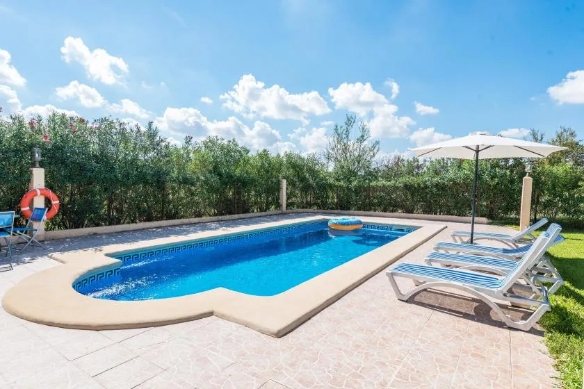 Una piscina al aire libre está rodeada por una terraza pavimentada y tumbonas.