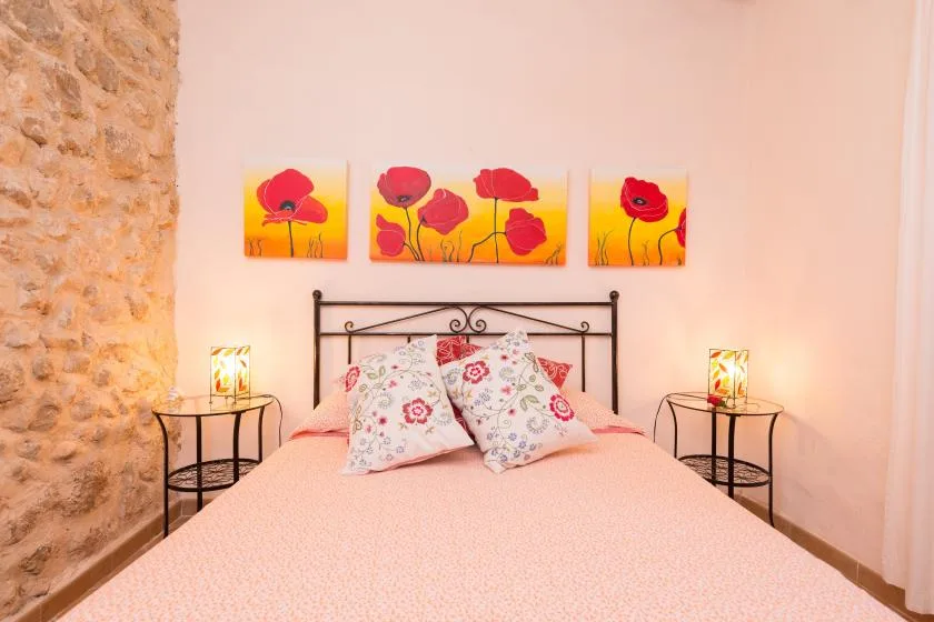 Un dormitorio con una cama, cojines florales y cuadros de amapolas sobre el cabecero.