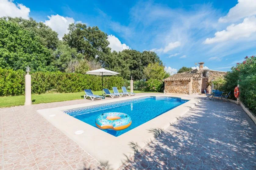 Una piscina al aire libre está rodeada de pavimento, vegetación y asientos reclinables.
