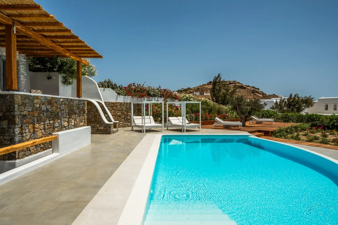 An outdoor swimming pool beside a stone terrace and shaded seating area.