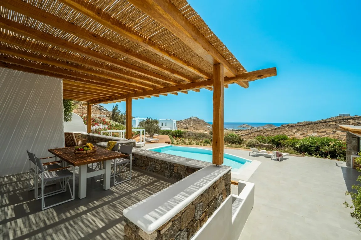 A shaded outdoor dining area overlooks a pool and the sea.