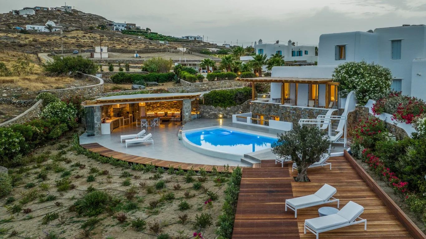 A hillside villa has a swimming pool, outdoor seating, and a wooden deck.