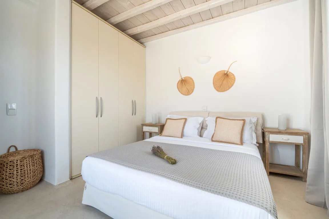A bright bedroom with a bed, built-in wardrobes, and woven wall decor.