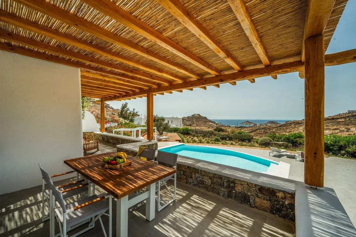 A covered outdoor dining area overlooks a swimming pool and the sea.