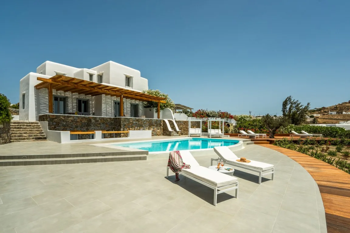A modern white villa overlooks a swimming pool and a broad paved terrace.
