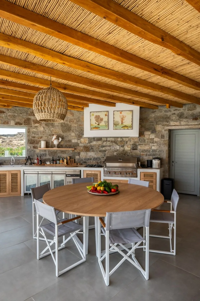 A stone-walled kitchen and dining area with a round table and exposed wooden beams.