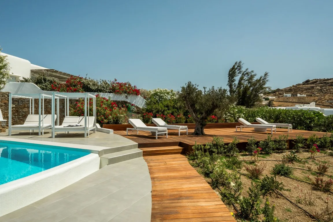 A swimming pool beside a wooden deck, lounge seating, and a landscaped garden.
