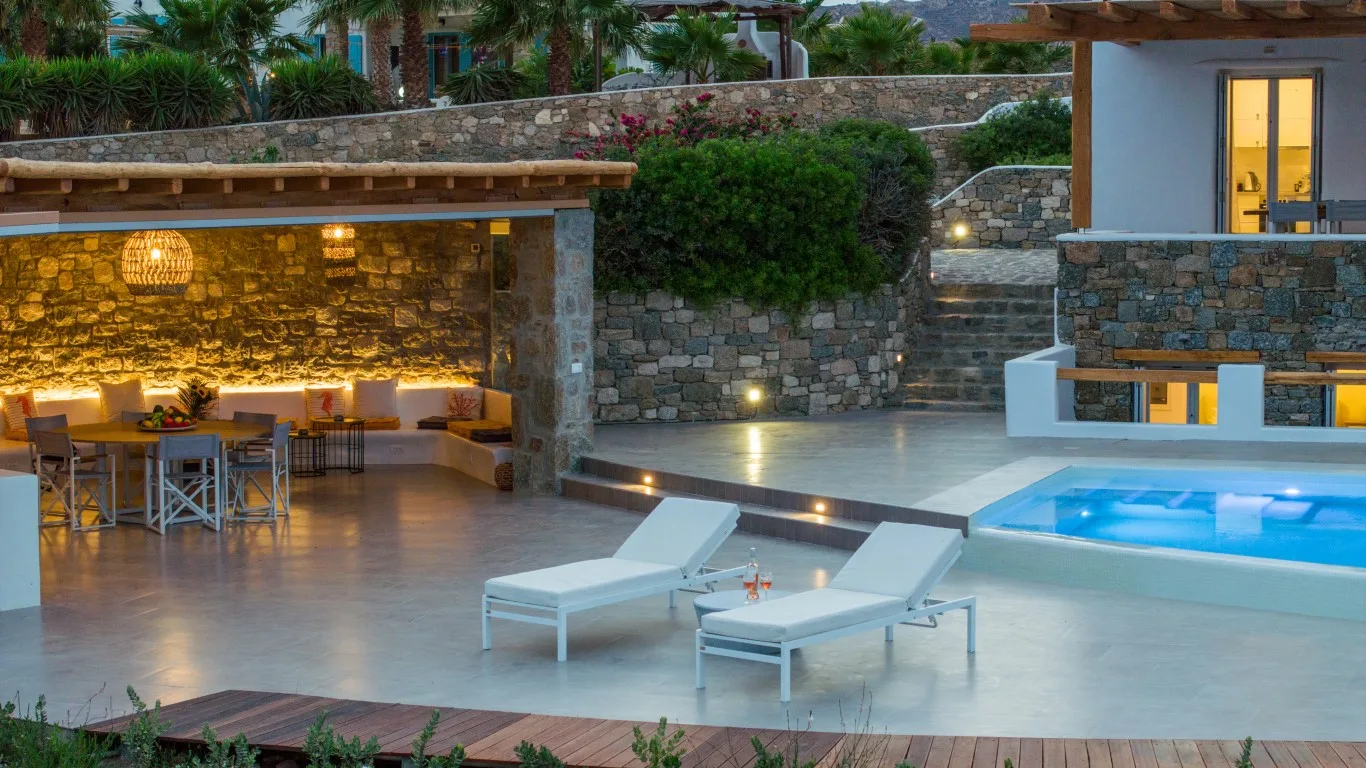 An outdoor pool and lounge area beside a stone dining space.